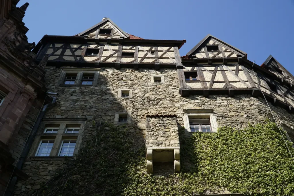 Kamienna elewacja zamku z charakterystycznymi drewnianymi konstrukcjami szachulcowymi i roślinnością porastającą mury, historyczna architektura Książa widziana od strony zamkowych tarasów