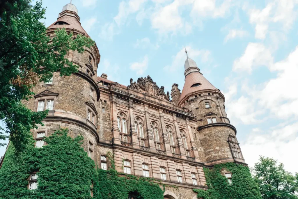 Kamienne wieże i bogato zdobiona fasada zamku porośnięta zielonym bluszczem, architektoniczne detale historycznej rezydencji Hochbergów i ślady wielowiekowych przebudów