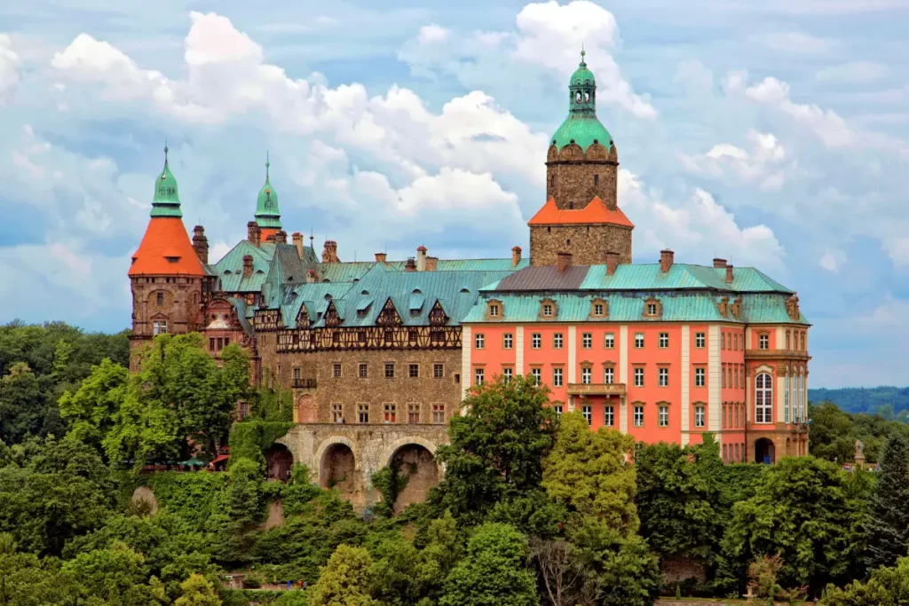 Panorama Zamku Książ z charakterystycznymi wieżami i kolorowymi fasadami wznoszącymi się ponad koronami drzew, największy zamek Dolnego Śląska i jego najciekawsze atrakcje turystyczne